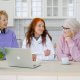 Three seniors having coffee in a kitchen with a laptop open.