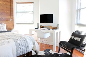 Bright dorm room with white walls, a window, partial view of the bed, and a desk, PC and chair.